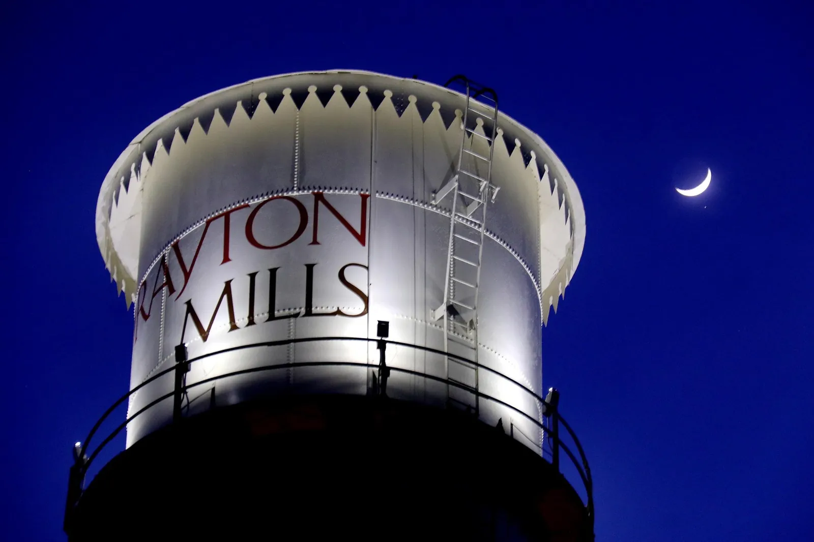 The lit Drayton Mills water tower against the night sky with a crescent moon