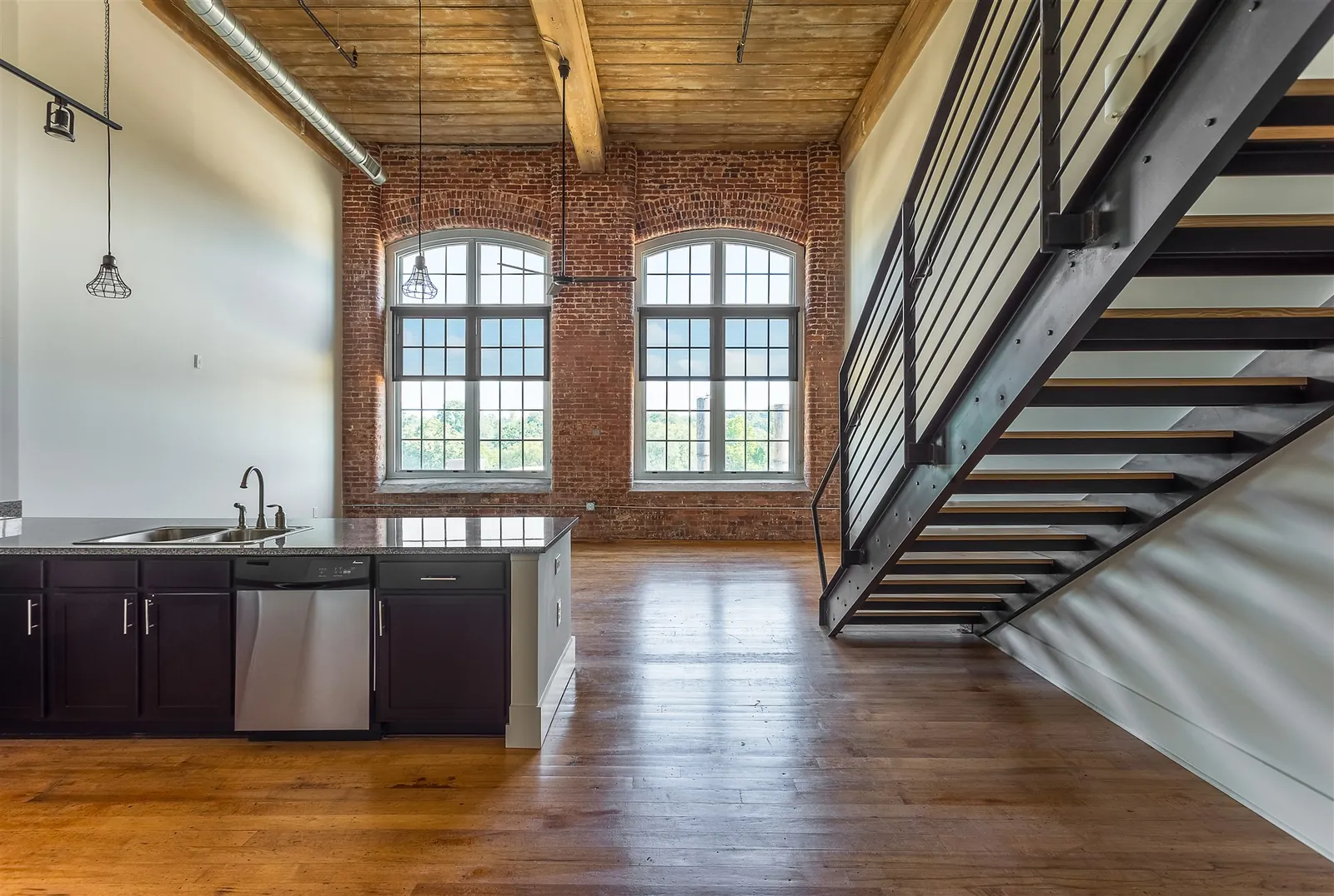 Steel staircase rising to the loft level of a three bedroom loft at Drayton Mills Lofts, with original hardwood floors and arched mill windows